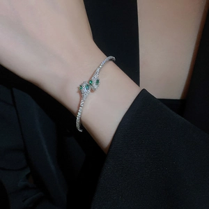 Detailed view of snake-style open cuff bracelet with white zircon and green gem eyes