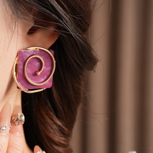 Close-up of vintage square earrings with purple enamel and golden spiral on model