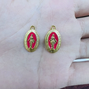Close-up of two red enamel religious medals with golden embossed Mary portraits