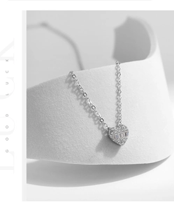 Macro shot of silver heart pendant with baguette zircons on a minimalist white stand