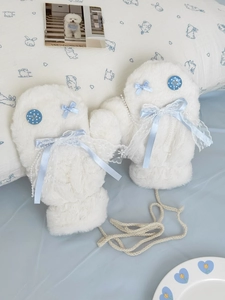 Detail of plush mittens with blue bow, lace trim, and pearl beads on soft white faux fur