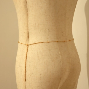 Close-up of minimalist gold beaded waist chain on mannequin with refined metallic finish