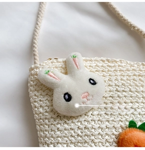 Dettaglio della borsa a tracolla intrecciata beige con coniglio di peluche e ricami