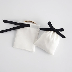 Detailed shot of white jewelry pouches with black ribbon bows and a gold bracelet