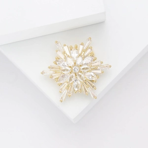 Elegant gold snowflake brooch with micro-paved zircons on a white geometric stand