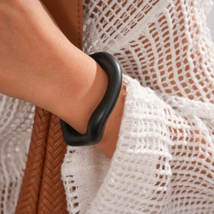 Close-up of minimalist black matte wavy acrylic cuff bracelet on a model's wrist