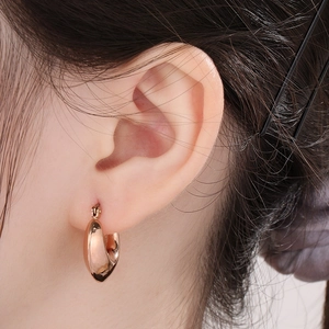 Macro shot of rose gold heart-shaped hoop earring on ear with polished mirror finish