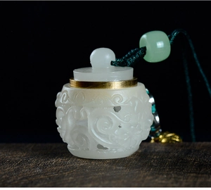 Detail of white jade-textured hollow carved sachet pendant with green bead and golden clasp