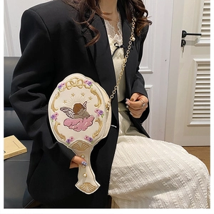 Detail of embroidered angel motifs on a mirror-shaped crossbody bag with gold chain strap