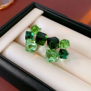 Detailed view of square green crystal stud earrings with silver needles in a jewelry box
