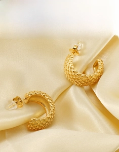 Détail de boucles d'oreilles créoles dorées 18K avec une fine texture géométrique grillagée