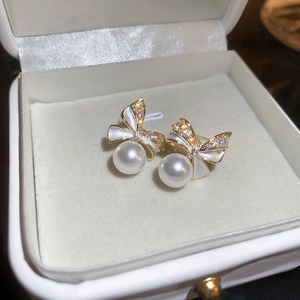 Golden bow earrings with white enamel, zircon accents and pearls in a jewelry box