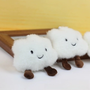 Close-up of white fluffy cloud plush keychain with embroidered smiley face and limbs