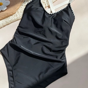 Detail of black one-piece swimsuit with white scalloped trim and crisscross straps