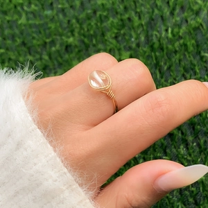 Detailed view of handmade gold wire-wrapped ring with a clear oval gemstone on green grass