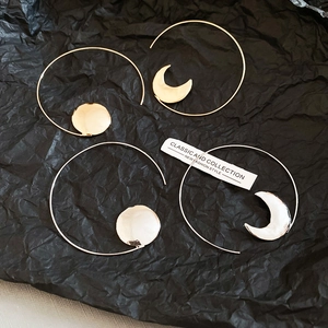 Macro shot of gold geometric sun and moon hoop earrings on a black textured backdrop