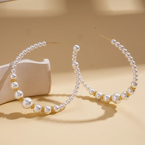 Elegant C-shaped pearl hoop earrings with gold spacer beads on a stone background