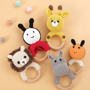 Five handmade crochet animal rattles for babies with natural wooden rings on beige background