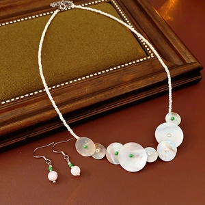 Detail of shell necklace and pink crystal earrings on a rustic dark wood surface