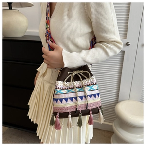 Detail of woven straw bucket bag featuring colorful embroidery and tassel accents