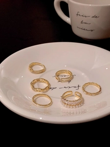 Detail view of a 6-piece set of golden open rings with pearls and zircon on ceramic plate