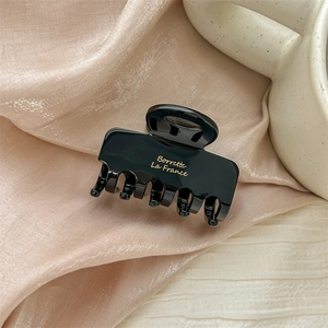 Close-up of black resin hair claw clip with gold Barrette La France script on satin