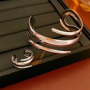 Detail von silbernem geometrischem Spiralarmreif und passendem offenem Ring auf Leder