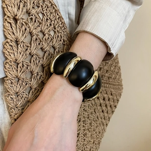 Close-up of wide acrylic bangle featuring matte black and polished gold geometric segments