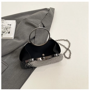 Detail of black evening bag featuring hammered texture and large metal ring handle