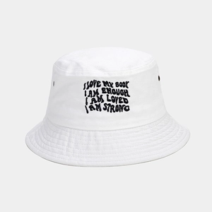 Detail of white cotton bucket hat featuring black slogan embroidery and metal eyelets