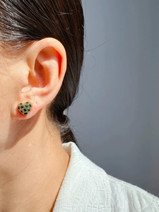 Close-up of heart-shaped gold stud earring with green gemstones on female ear