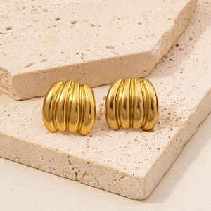 Detailed macro view of gold-tone irregular ribbed earrings on a textured stone base