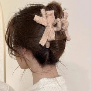 Beige knitted bow hair claw clip for women shown on a bun hairstyle with warm lighting
