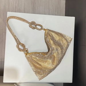 Close-up of golden rhinestone handbag featuring a decorative double knot shoulder strap