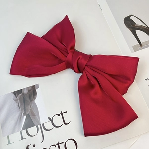 Close-up of wine red satin bow hair clip with textured fabric on magazine background