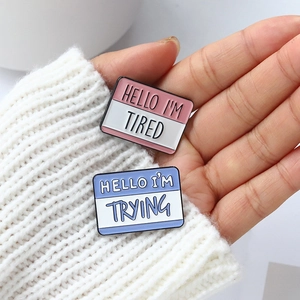 Metal enamel pins set featuring Hello I'm Tired and I'm Trying on a white knit sweater