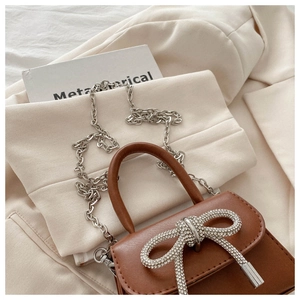 Close-up of brown leather bag featuring a large silver rhinestone bow and chain strap