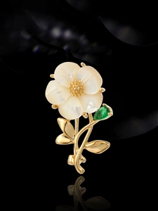 Detail of shell flower brooch with gold petals, green gemstone leaf and reflection