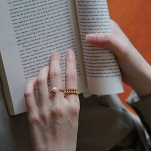 Classic gold pearl ring and chain band worn while reading a book in warm lighting