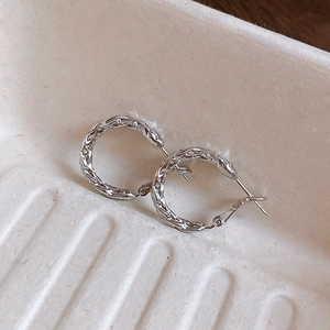 Detailed close-up of silver twist hoop earrings with intricate woven metal texture