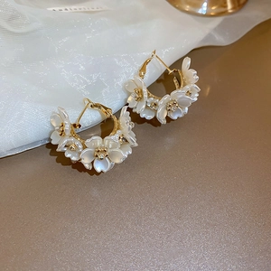 Detail of floral C-shaped hoop earrings with white petals and sparkling rhinestones