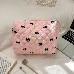 Close-up of pink quilted cosmetic bag with black cat print on a white bed background