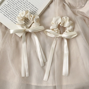 Elegant set of cream satin scrunchies with long ribbons on a soft aesthetic background