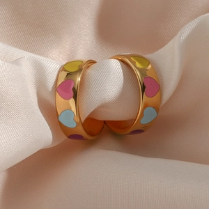 Macro detail of gold hoop earrings featuring colorful enamel heart patterns on satin