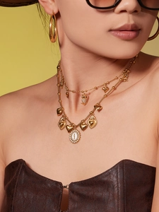 Detail shot of layered gold owl and heart charm necklaces with large hoop earrings