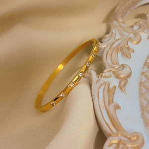 Elegant gold titanium steel bangle with inlaid zircons on a textured cream background