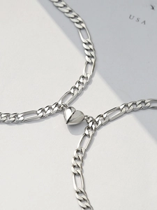 Close-up of silver Figaro link couple bracelets featuring a magnetic heart-shaped clasp