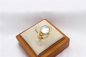 Detail of a gold signet ring featuring a round white mother of pearl inlay on a jewelry stand