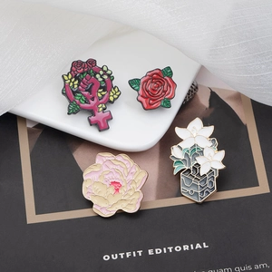 Detail of floral enamel brooches including pink peonies and roses on soft white fabric