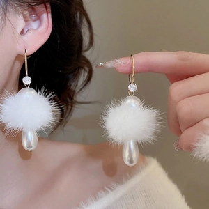 Elegant gold earrings with white fur balls and teardrop pearls shown on a model